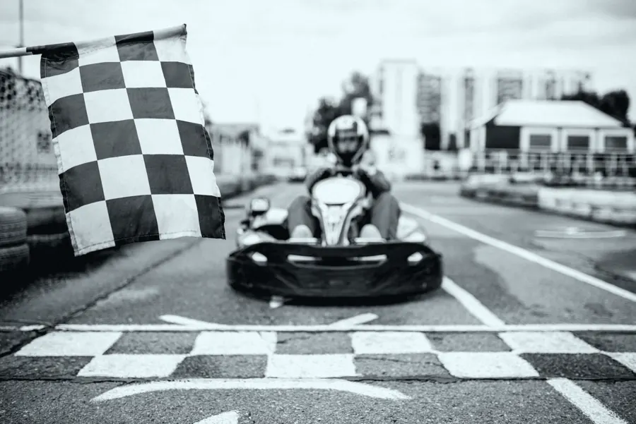 Kart cruzando a linha de chegada sob a bandeira quadriculada.