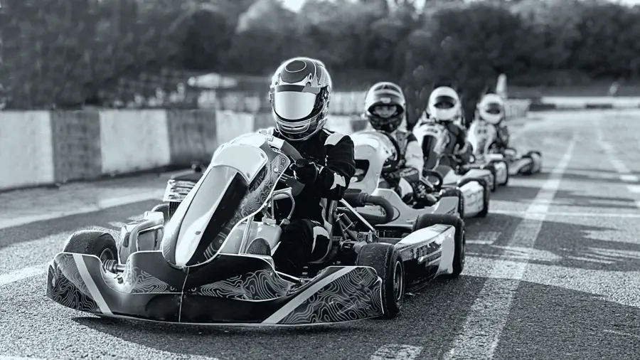 Fila de karts alinhados no grid de largada, pilotos de capacete, em foto preto e branco.