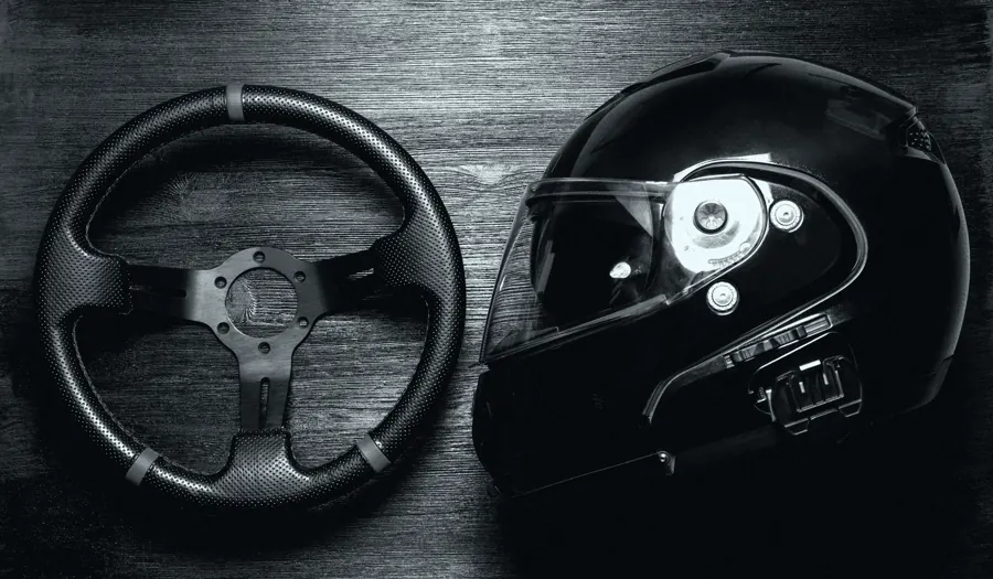 Volante de kart e capacete preto apoiados sobre uma mesa de madeira.